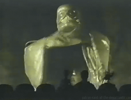 TV gif. From Mystery Science Theater 3000, three characters sit in a theater viewing a screen showing a large, golden, sage-like figure slowly opening its arms wide. Text, "Join us!"