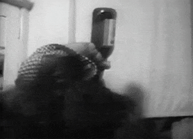 Celebrity gif. Black and white footage of Charles Bukowski taking a deep swig from a liquor bottle, then exhaling as he leans forward.