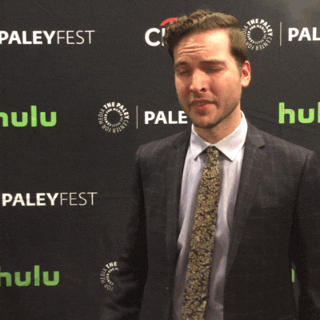 Celebrity gif. Man at PaleyFest being interviewed and he hears good news. He scrunches his face tightly and does a fist pump in happiness.