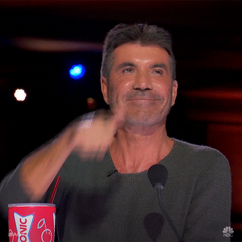 Reality TV gif. Simon Cowell on America's Got Talent, smiles and gives an energetic thumbs up.