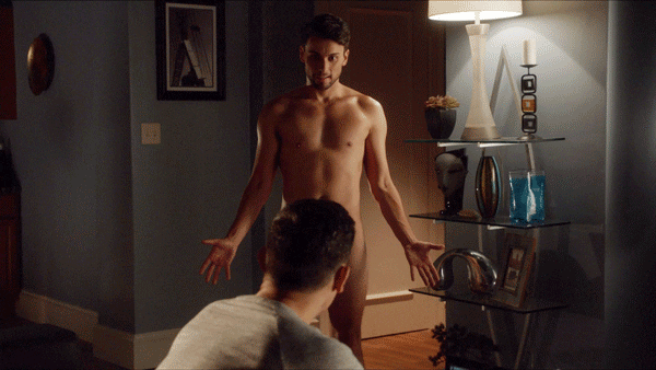 TV gif. Jack Falahee as Connor in How to Get Away with Murder stands nude in a living room with his palms out by his side, in front of a man whose head blocks our view of his crotch.