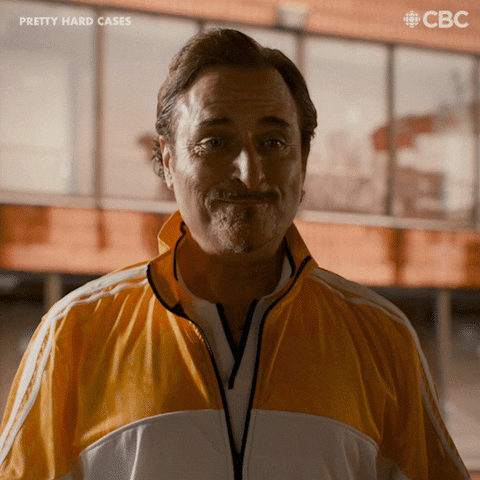 TV gif. Kim Coates as Bill in Pretty Hard Cases is dressed in gym clothes and he is munching on something, very unbothered by anything going on. He shrugs and jovially says, "It's Friday!"