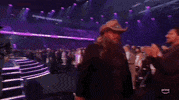 Academy of Country Music Awards gif. Chris Stapleton walks past standing audience members with a pleased look on his face, nods his head to acknowledge a couple of people while nondescriptly saying something.