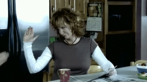 TV gif. Smiling Reba McEntire on Reb gives her son a casual high five as he walks past her through the kitchen.