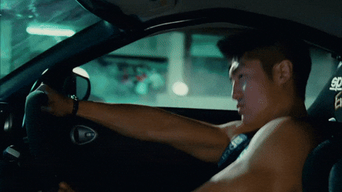 Movie gif. Brian Tee as DK in the Fast and the Furious Tokyo Drift sits behind a steering wheel as the black race car drifts sideways up a ramp. 