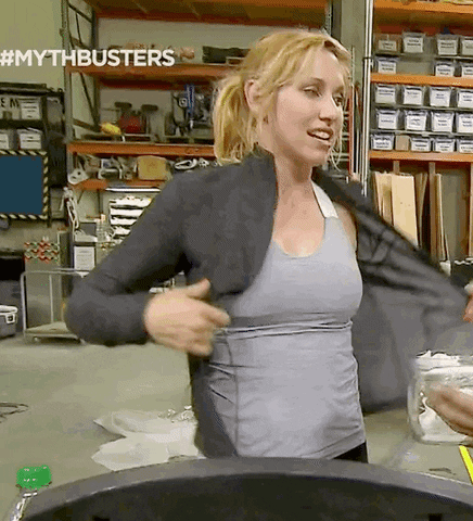 TV gif. Kari Byron from MythBusters strips off her sports jacket, which accentuates her slim figure, and exhales dramatically as sweat glistens off of her forehead and chest.