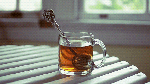 Video gif. Steam wafts from a transparent mug of tea with an ornate tea strainer resting inside.