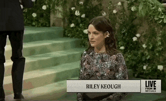 Met Gala 2024 gif. Riley Keough wearing a dark Chanel gown with an elaborate floral sequin pattern resembling jacquard, poses for the cameras.