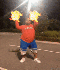 Video gif. In a parking lot at night, a young man in an orange hoodie and blue shorts performs a dance. Special effects turn the dance into a parody of Avatar: The Last Airbender with fireballs resembling cheerleading pom-poms, spinning movements creating gusts of wind, a sudden wave of water, and stone blocks rising from the ground.