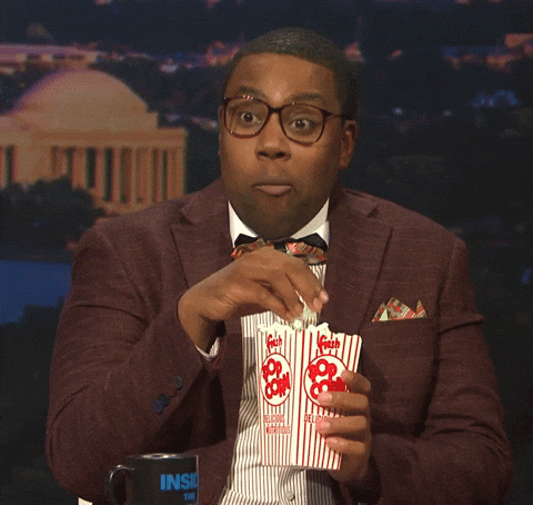 SNL gif. Kenan Thompson in thick rimmed glasses and a bow tie nods energetically while eating popcorn like he's excited or maybe a little anxious and intense.