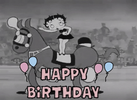 Cartoon gif. Betty Boop is standing on a horse that rides by and she blows kisses to the crowd. Text, "Happy Birthday!"