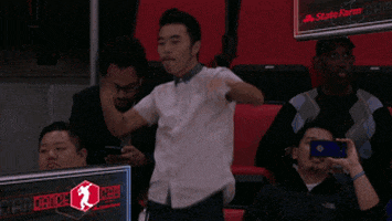 Video gif. A man is at a basketball game and has stood up to dance. The dance cam falls on him and he notices, which ups the ante for him and he dances even harder, rolling his hips and waving his arms in unison.