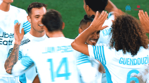 Sports gif. Teammates from Olympique de Marseille clap and embrace in celebration. 