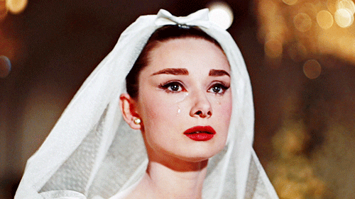 Movie gif. Audrey Hepburn as Jo Stockton in Funny Face sheds a tear from both eyes at the wedding ceremony.