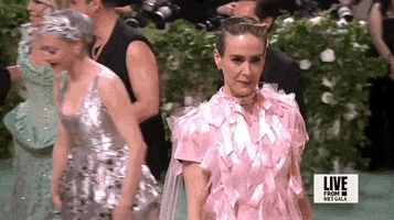 Met Gala 2024 gif. Slow motion clip of the top of Sarah Paulson's pale pink short-sleeved Prada gown covered in pale pink satin bows that catch the light and flutter as she walks.
