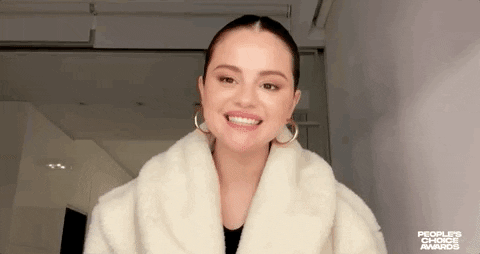 Celebrity gif. Selena looks at us with a big smile. She then covers her eyes with her hands as if waiting for a surprise.