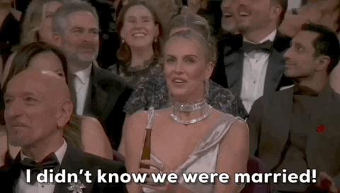 Oscars 2024 GIF. Charlize Theron, seated at the Oscars, clutches her chest, laughing in shock, exclaiming, “I didn’t know we were married.”