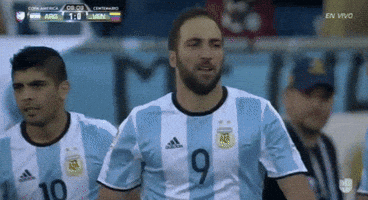 Sports gif. Gonzalo Higuain points at a teammate with both fingers as he walks toward him and then they do a double high-five. Argentina is up one to zero against Venezuela. 