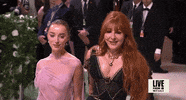 Met Gala 2024 gif. Slomo of Phoebe Dynevor wearing an ethereal Victoria Beckham gown, posing for the cameras holding hands with Charlotte Tilbury, adjust with an elegant tip of her chin.