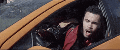 Music video gif. 99percent is leaning out his car window with his jaw dropped and his eyes are fixed on somebody walking by.