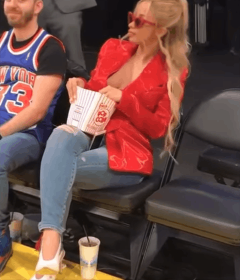 Celebrity gif. Cardi B at a basketball game bopping to the beat while enjoying her box of popcorn. 