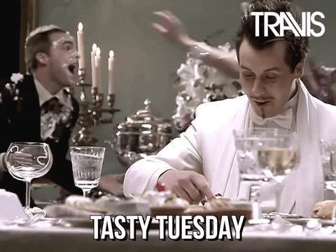 Celebrity gif. Oblivious to a chaotic wedding food fight going on around him, Neil Primrose dips his finger in his dessert and delights in tasting it. Text, "Tasty Tuesday."