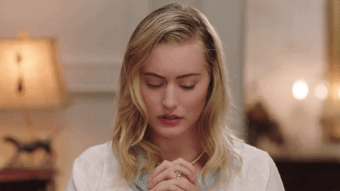 TV gif. Olivia Macklin as Becky in Filthy Rich bows her head over her interlocked raised hands in prayer.