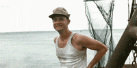 Movie gif. Tom Hanks as Forrest Gump laughs happily on the deck of a Bubba Shrimp boat before he sees something he's afraid of and ducks back behind cover. 