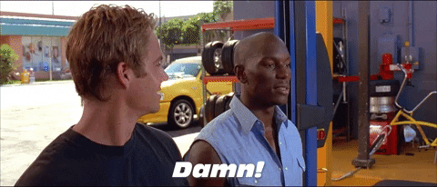 Movie gif. Paul Walker as Brian and Tyrese Gibson as Roman in 2 Fast 2 Furious. Roman looks at a car garage in awe and says, "Damn!" while Brian grins widely at him and heads in.