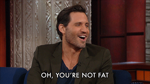 Celebrity gif. Late Show with Stephen Colbert guest Edgar Ramirez, smiles and shakes his head, saying "oh, you're not fat."