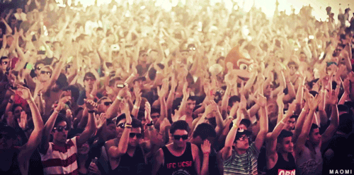 Video gif. A crowd of people at a music concert clap and bang their heads to the music. 