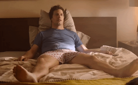Movie gif. Comedian Andy Samberg as Nyles in Palm Springs sits splayed out in bed and gives a sarcastic thumbs up.