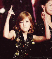 Celebrity gif. Taeyeon looks at us sternly while giving us the finger with both hands, holding a mic in one hand.