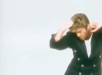 Celebrity gif. In a retro music video, an excited George Michael dances happily wearing a black suit.