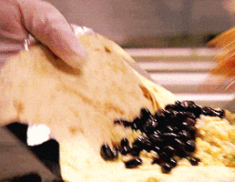 Video gif. A hand holds an open tortilla as another tosses seasoned meat over black beans. 
