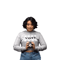 Video gif. Woman wearing a shirt with the word “Voter” shakes a Magic 8 ball in front of herself against a transparent background. Gold stars appear around her as she reads the prediction. She smiles, and the prediction appears above her head in a blue triangle with the message, “I will be vote ready.”