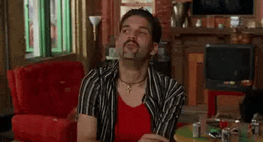 Movie gif. Guillermo Diaz as Scarface in Half Baked looks suddenly surprised and points forward at something while holding a joint.