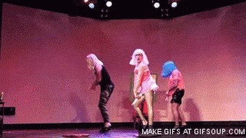 Video gif. Three people dance on stage with wigs on their heads. They do the famous Single Ladies dance, bending forward and bending their knees. They step side to side, out of unison.