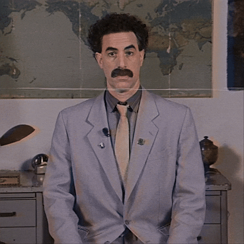 Movie gif. Sacha Baron Cohen as Borat sits in front of a map and raises his two thumbs, waggling his eyebrows and giving an approving nod and toothy grin. (Added via Giphy)