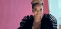 Celebrity gif. Rihanna, wearing a billow-sleeved black dress, smiles and covers her face with her hands like she's slightly embarrassed.