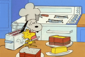 Peanuts gif. Wearing a chef’s hat, Snoopy is busy making a stack of buttered toast in the kitchen with Woodstock. Snoopy accidentally drops his ear in the toaster and his ear begins to burn. He pulls it out and Woodstock begins to butter his ear as if it is a piece of toast, then Snoopy pulls it away in annoyance.