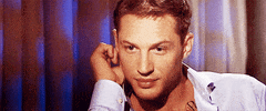 Celebrity gif. Tom Hardy looks up at us with a sexy gaze as he holds his hand near his ear. He then winks at us flirtatiously.