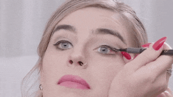 Video gif. Christina Wolfgram carefully puts on eyeliner as the black liner marks unevenly across her eyelid. Text, "Oops."