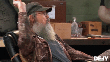 Reality TV gif. Si Robertson sits back, reclined in an office chair. He holds his hand up with an imaginary whip in it. He circles the invisible whip around and cracks it, making the sound effects with his mouth. 