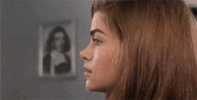 Movie gif. Denise Richards as Captain Carmen in Starship Troopers looks over at us and smiles. 