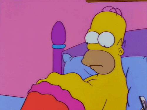 The Simpsons gif. Homer lays in bed staring down at his protruding belly as it jigglies in waves. 