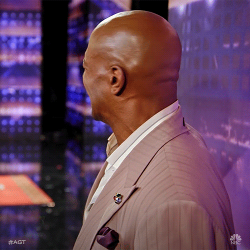Reality TV gif. Terry Crews on America’s Got Talent looks at the stage and turns towards us squinting his face and grimacing.