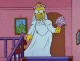 The Simpsons gif. Dressed in a white wedding dress, Homer takes a step down the stairs and pauses to smell his bouquet.