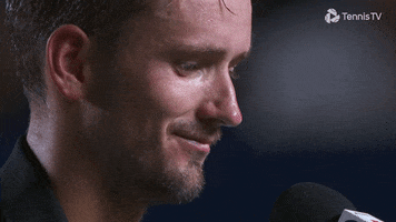 Sports gif. Daniil Medvedev, a Russian tennis player, taps a microphone with one finger, smiling down and saying, "Hello," into the mic.