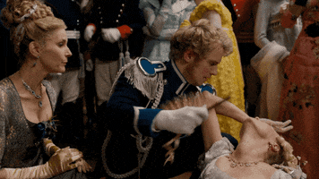 TV gif. Jessica Madsen as Cressida Cowper from Bridgerton has fainted on the dance floor and Freddie Stroma as Prince Friedrich is holding her. He fans her quickly, trying to rouse her, and her hand is on her forehead as she smiles at him while coming to.